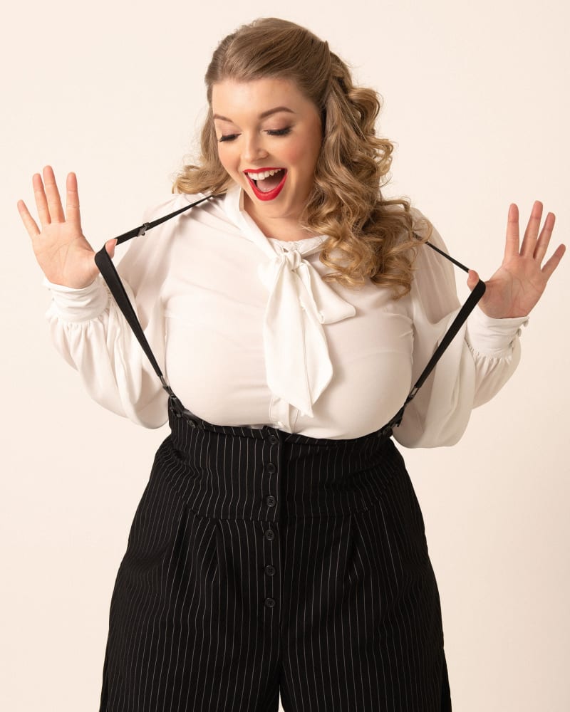 Side of a model wearing a size 4X/22-24 Unique Vintage Plus Size Black & White Pin Stripe Thelma Suspender Pants in Black & White Pin Stripe by Unique Vintage. | dia_product_style_image_id:269954